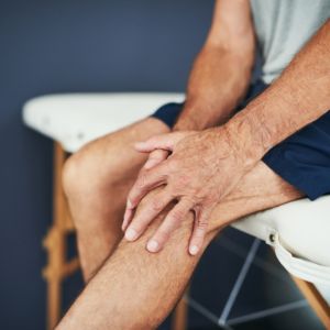 A person sits on a bench, wearing shorts and holding their knee with both hands, suggesting possible knee discomfort or pain—perhaps seeking help from a Chiropractor in Lower Manhattan.