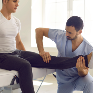 A Chiropractor in Lower Manhattan examines a patient's leg, bending it at the knee, in a medical or physical therapy setting.