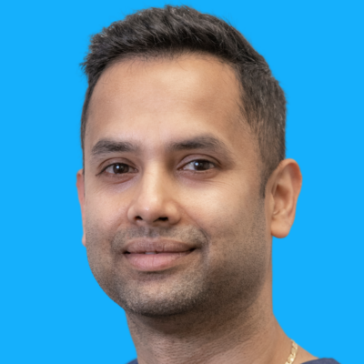 Chandan Debnath - Acupuncture A man with short dark hair and trimmed facial hair is smiling slightly, shown against a solid bright blue background.