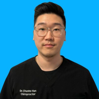 Dr. Chanho Han - Chiropractor A man wearing clear glasses and black scrubs labeled "Dr. Chanho Han Chiropractor" stands against a solid blue background.