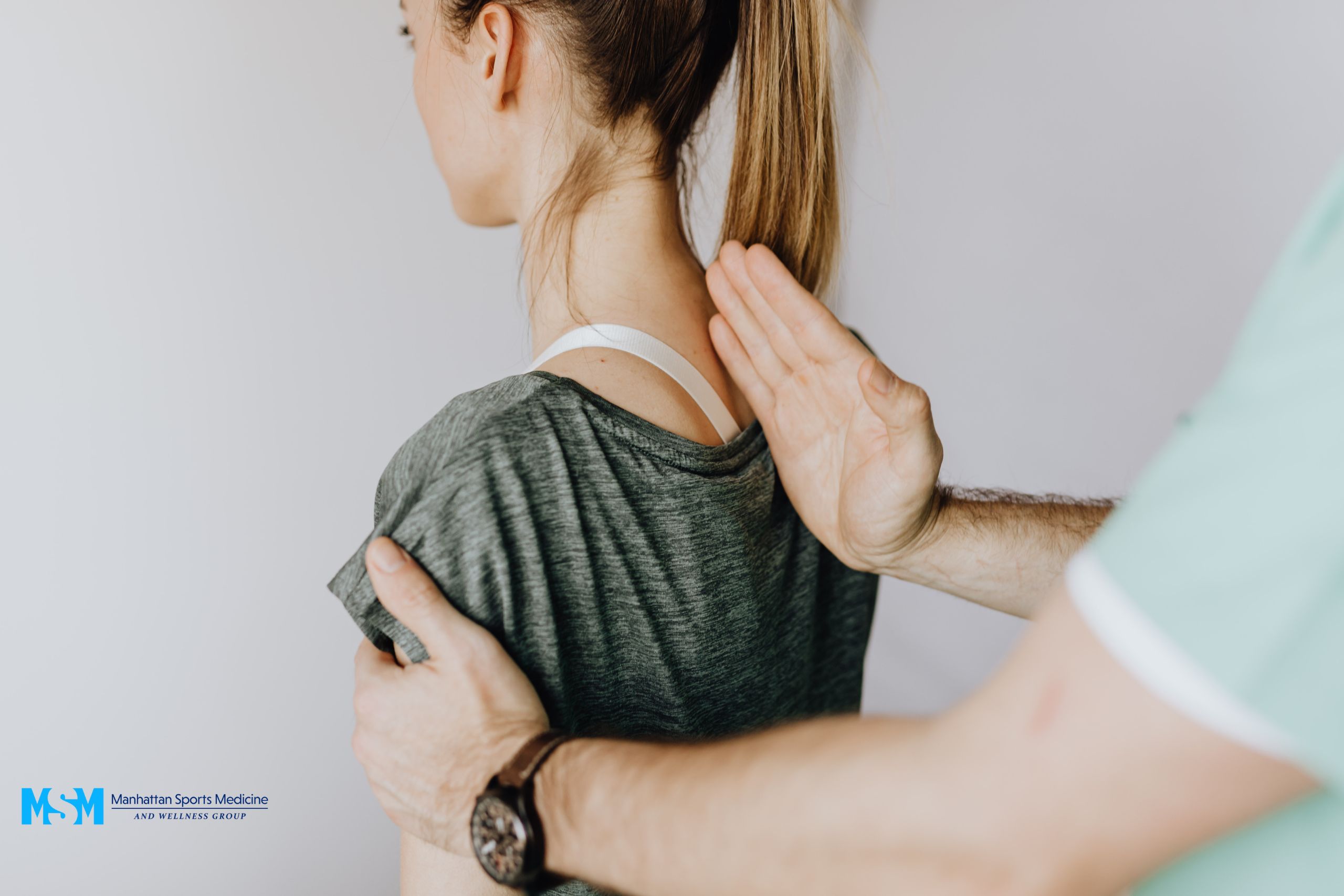 Person in a gray shirt being assessed by a healthcare professional, who is touching their shoulder and neck. Person in a gray shirt being assessed by a healthcare professional, who is touching their shoulder and neck