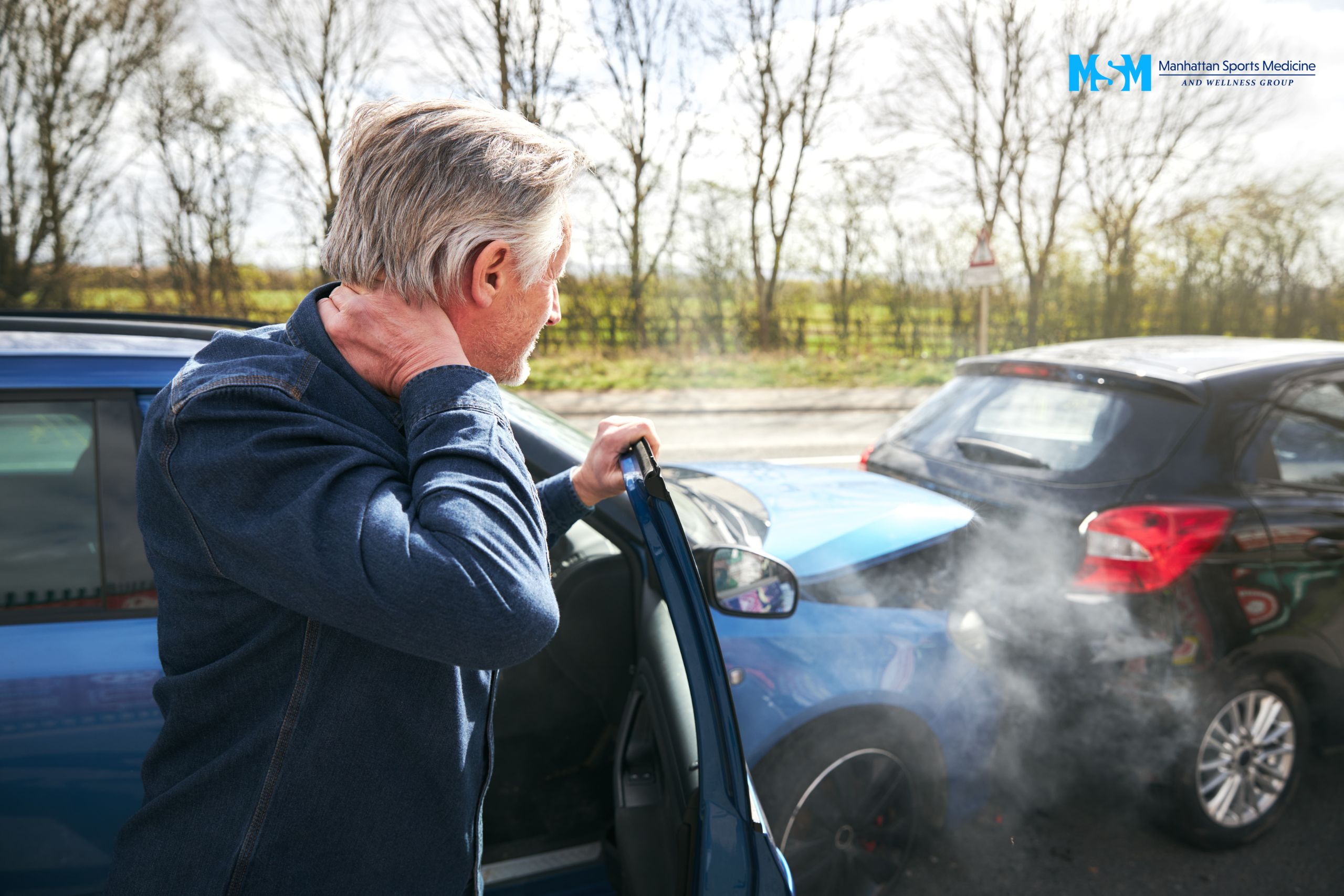 Man stands outside a blue car holding his neck, looking at the rear-end collision with a black car; both vehicles are damaged and emitting smoke. Man stands outside a blue car holding his neck, looking at the rear end collision with a black car; both vehicles are damaged and emitting smoke